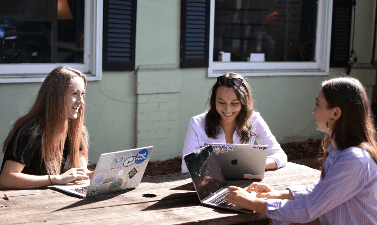 Three students sitting on a bench in front of Forge smiling